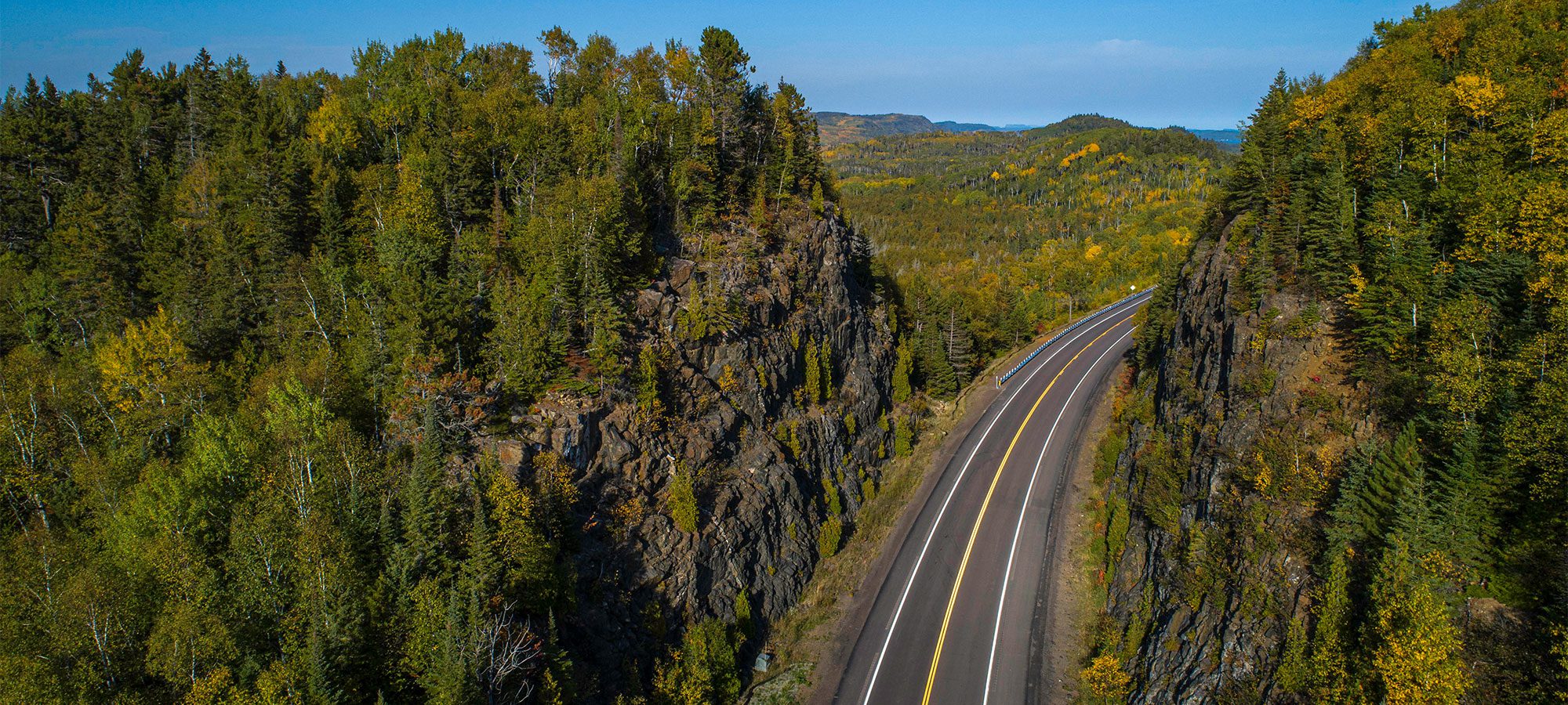aerial view of highway lined with forest and rocks