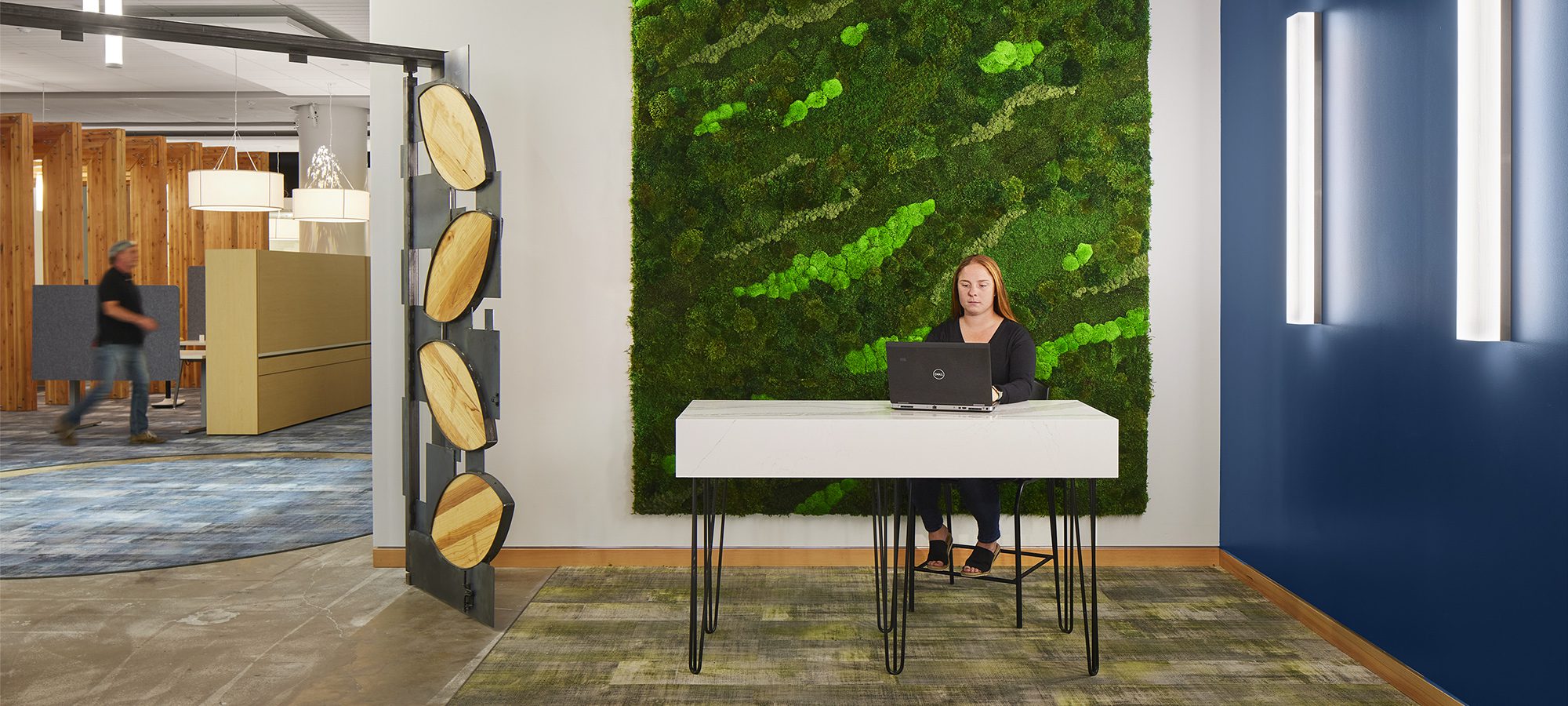 a woman sits at a desk in front of a moss wall