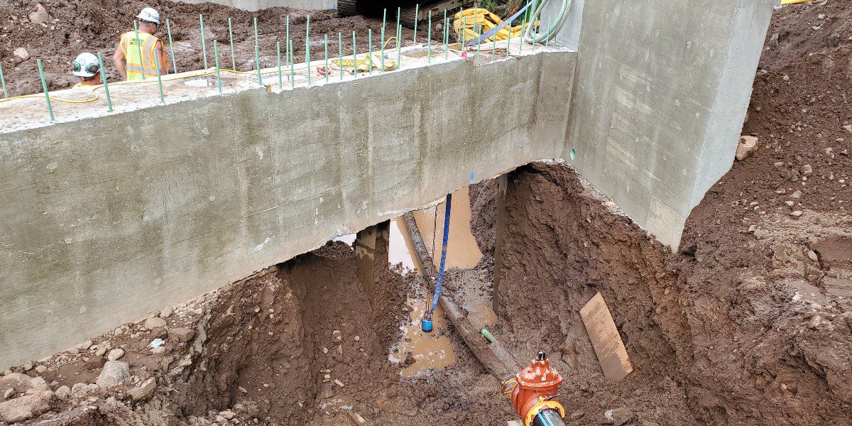 Pipe being installed in earthen pit under a concrete beam
